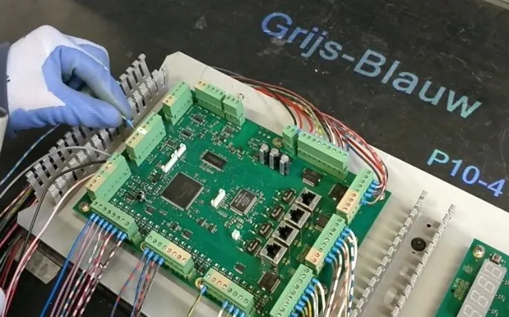 Operatore che collega fili colorati ai morsetti di un circuito stampato, con un codice colore proiettato sul piano di lavoro
