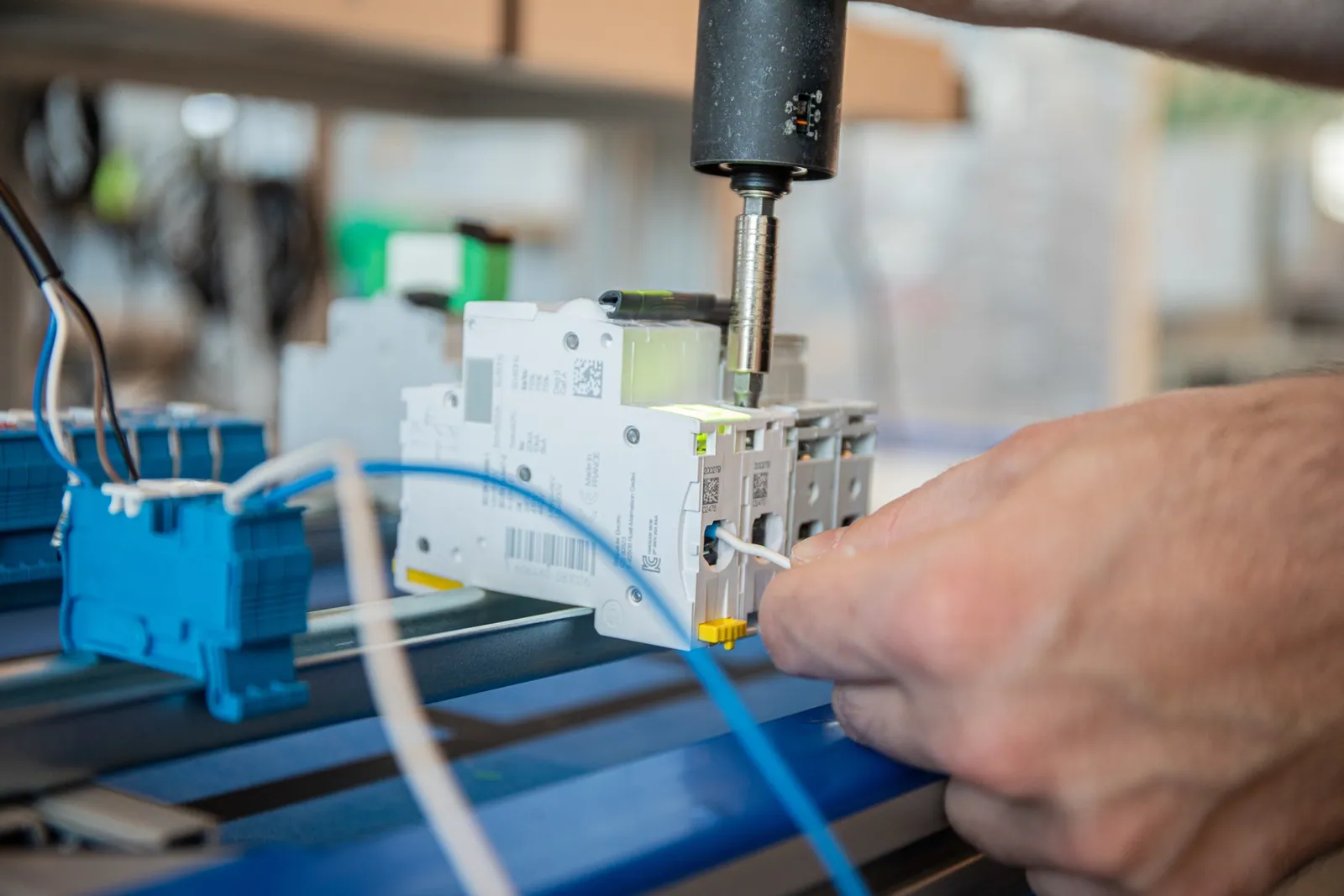 Visseuse connectée serrant une borne sur un disjoncteur pendant que l'opérateur positionne un câble, avec une mise en évidence projetée sur la cible