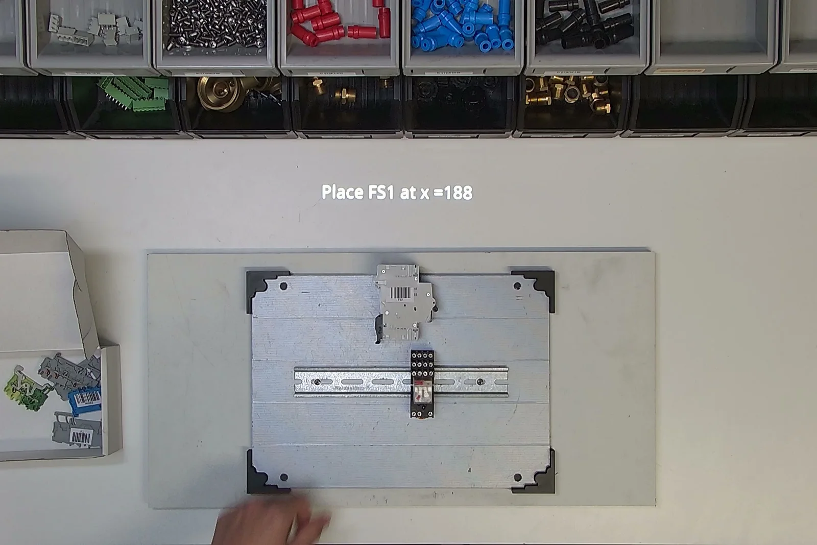 Control cabinet demo at an Arkite workstation: the instruction 'Place FS1 at x=188' is projected with the exact position on the DIN rail